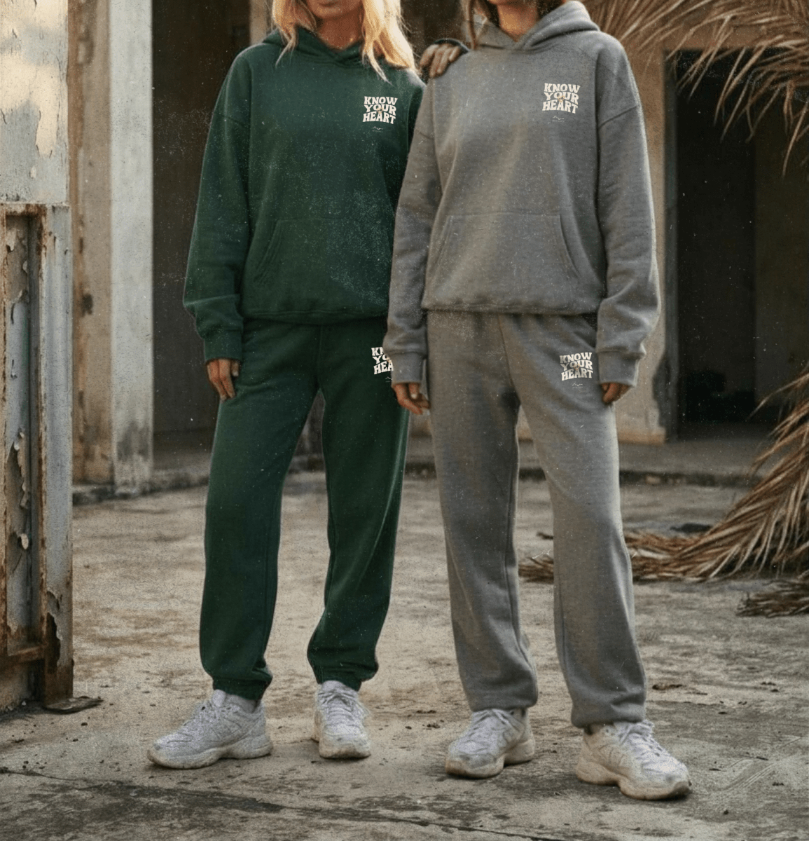 Two people wearing green and gray tracksuits with a logo on a rustic background