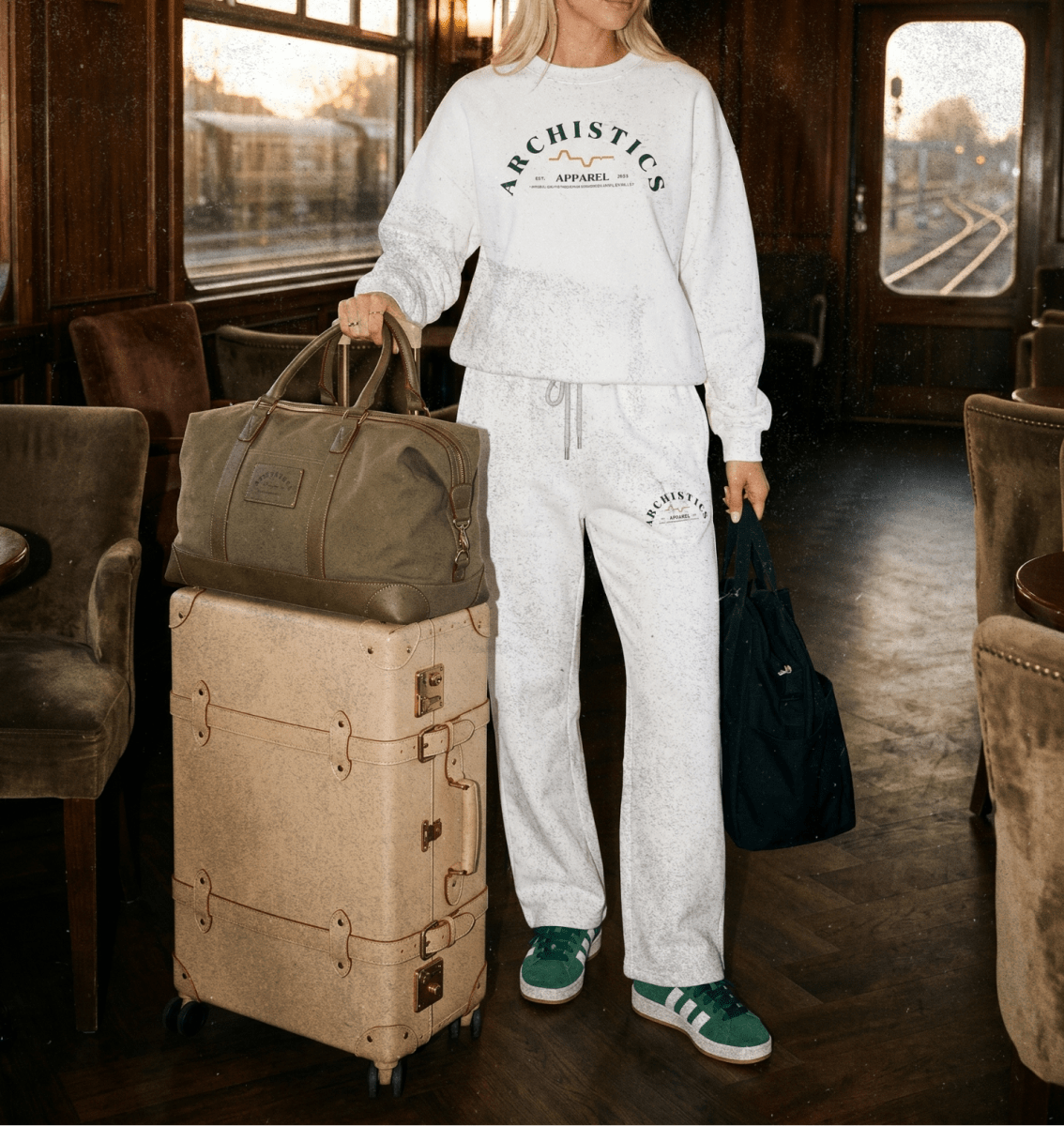 Person in a white tracksuit with 'Archistics' logo, standing in a train carriage with luggage.