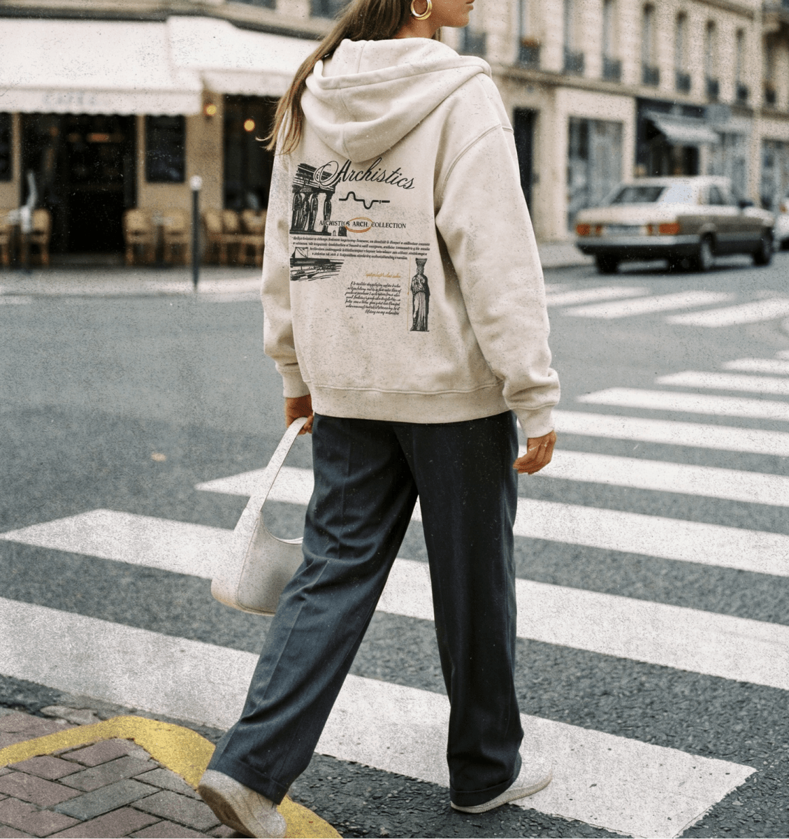 Person wearing a beige hoodie with graphics and text, walking on a city street.