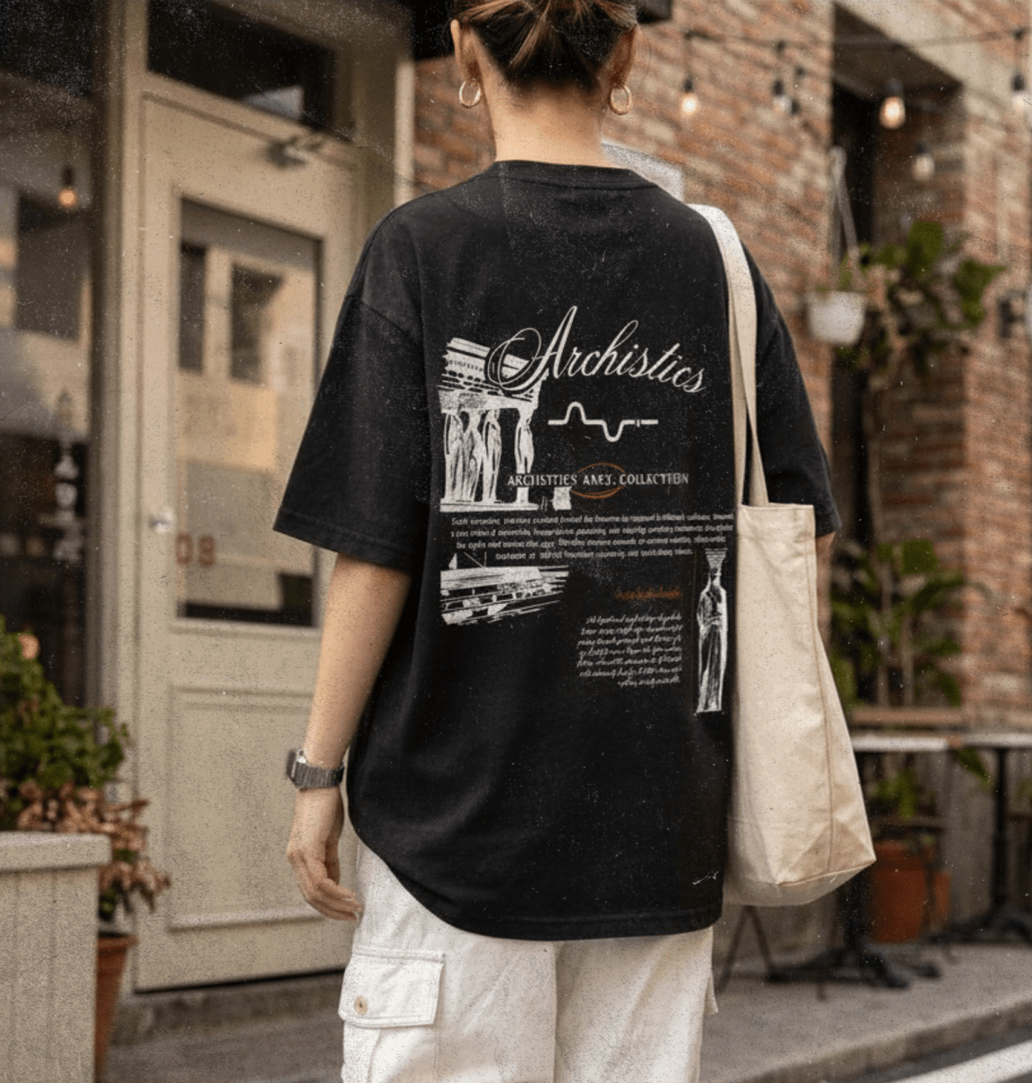 Person wearing a black t-shirt with graphics and text, standing on a street.