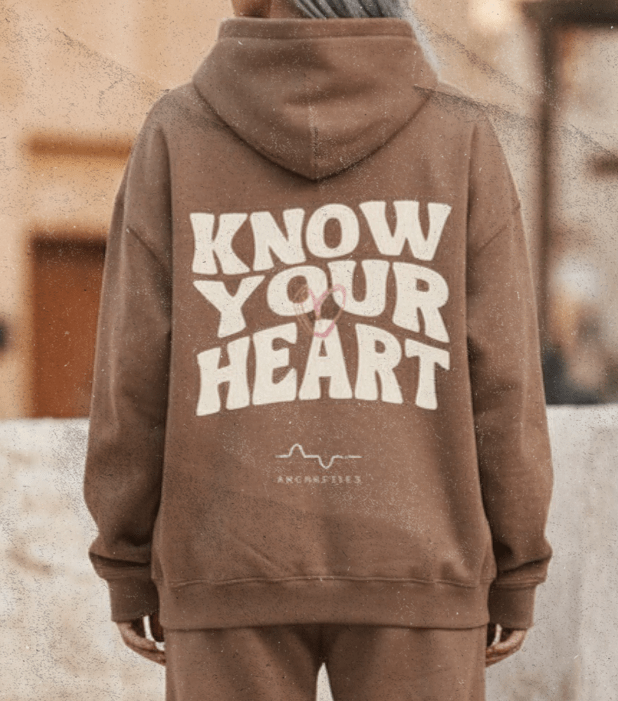 Person wearing a brown hoodie and pants with 'Know Your Heart' text, standing outdoors.