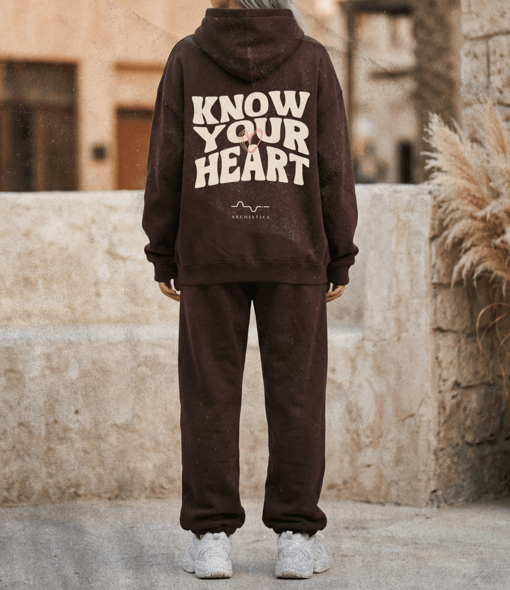 Person wearing a brown hoodie and pants with 'Know Your Heart' text, standing outdoors.