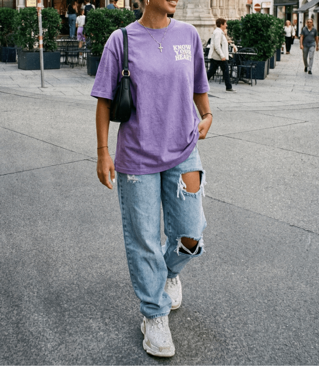 Person wearing a purple t-shirt and ripped jeans on a city street.
