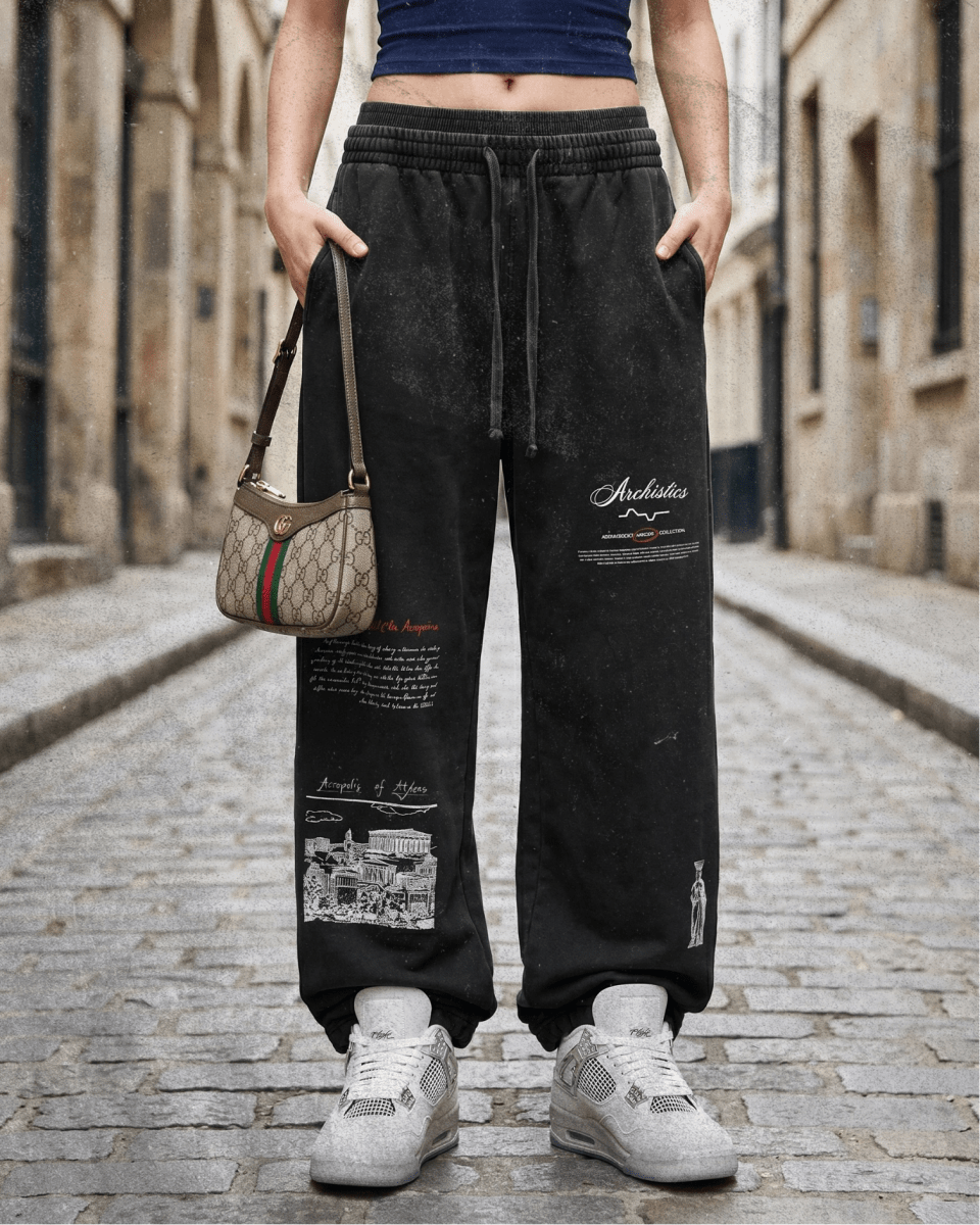 Person wearing black pants with text and graphics, standing on a street.