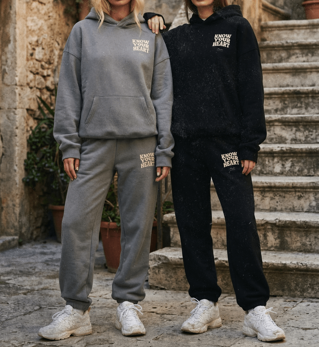 Two people wearing matching gray and black tracksuits with text on a stone staircase.