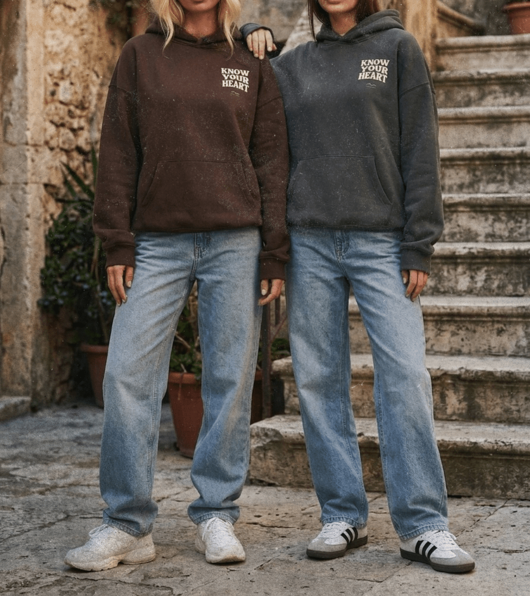 Two people wearing matching hoodies and jeans standing on stone steps.