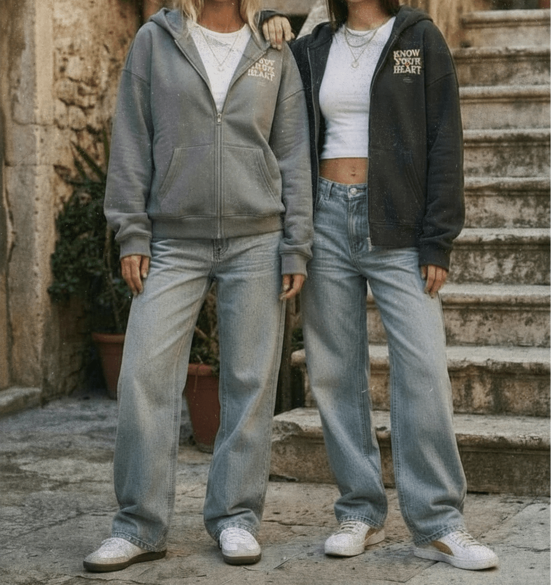 Two people wearing matching gray hoodies and light blue jeans standing on stone steps.