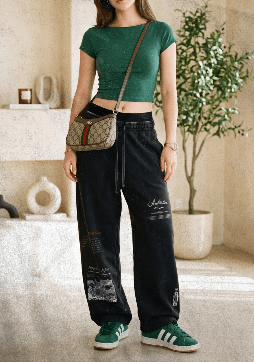 Woman in green top and black pants with a patterned bag in a room with decor elements.