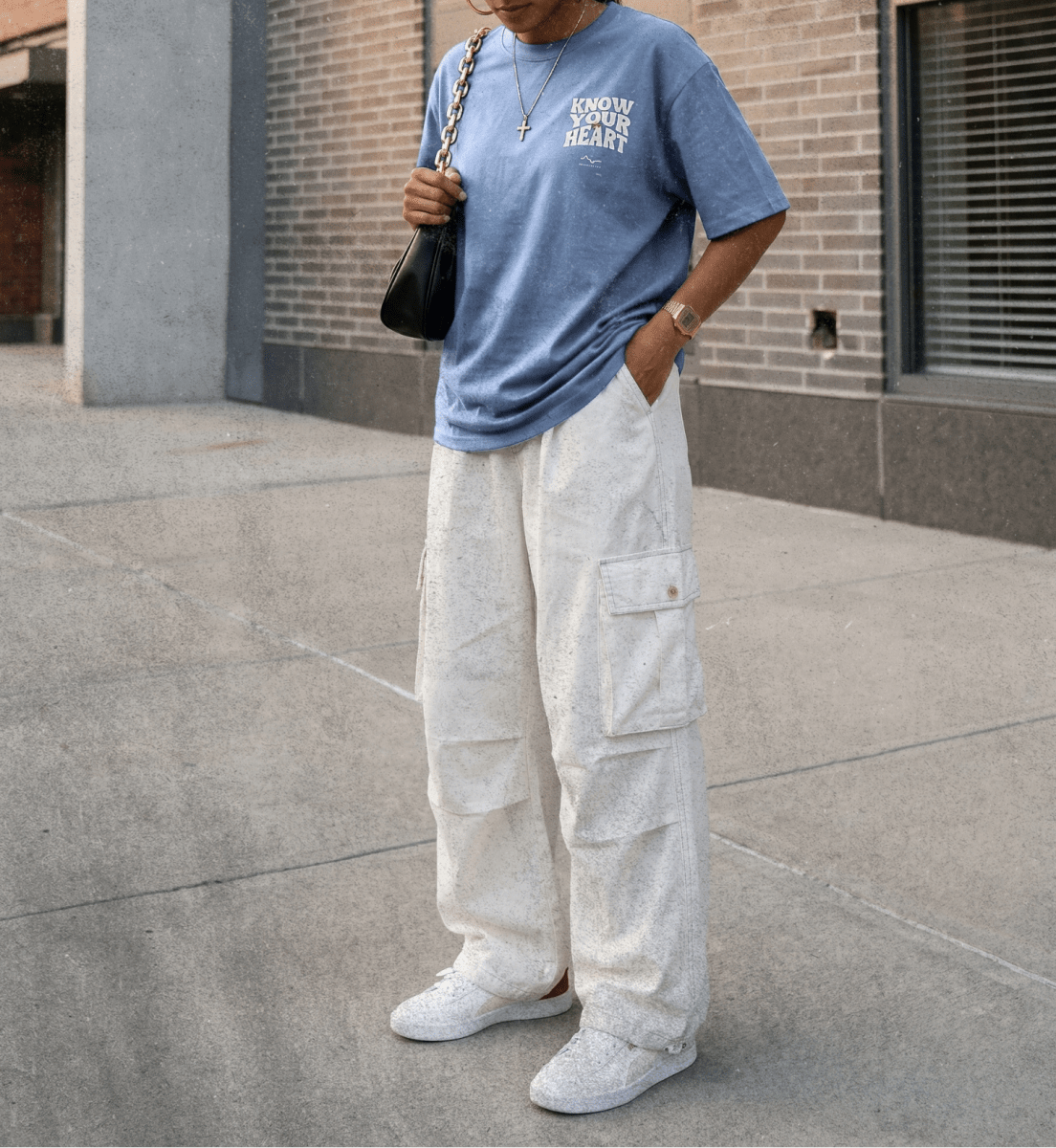 Woman wearing a blue t-shirt and white cargo pants standing on a sidewalk.