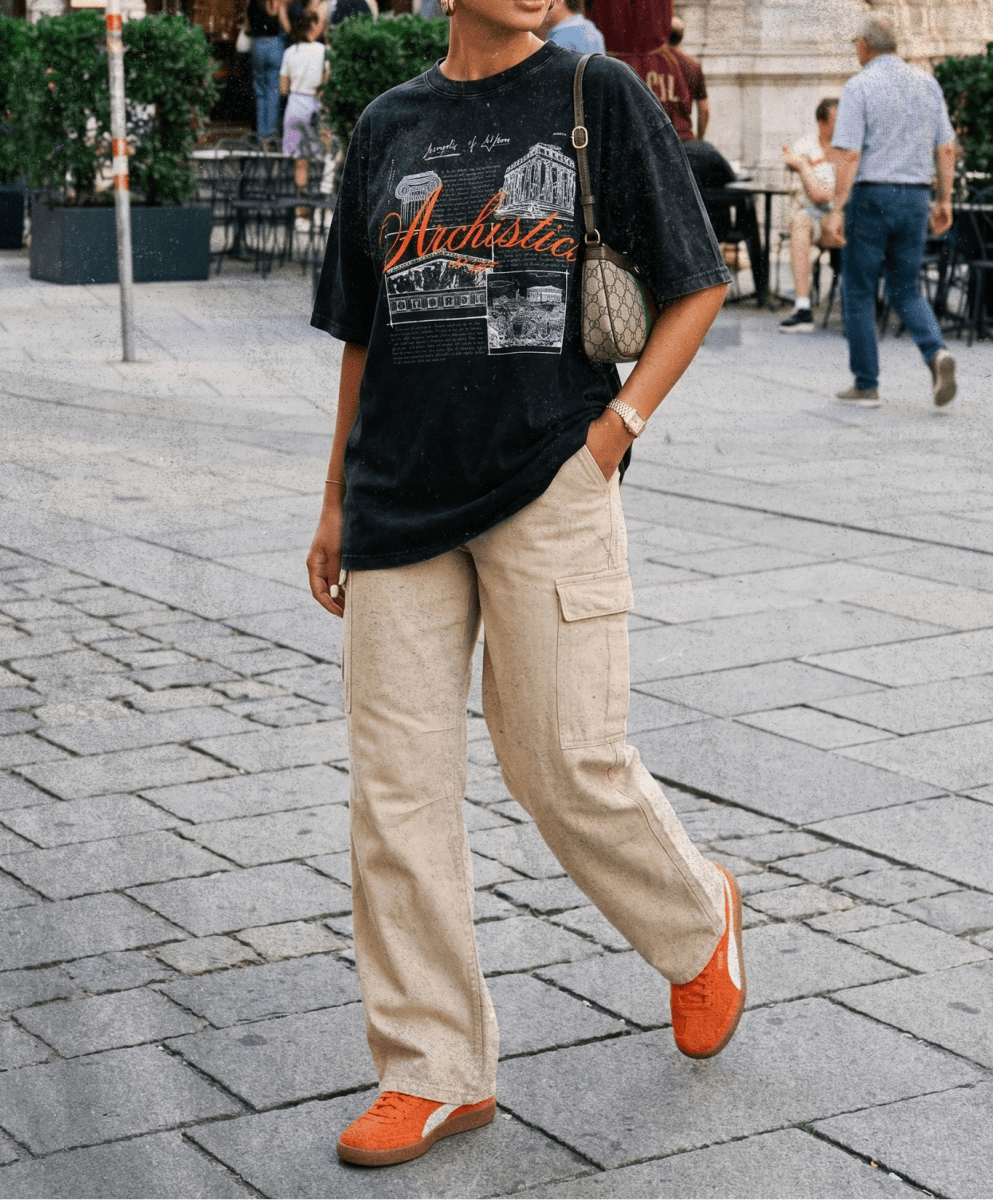 Woman wearing a black t-shirt with graphic design, beige pants, and orange shoes on a city street.