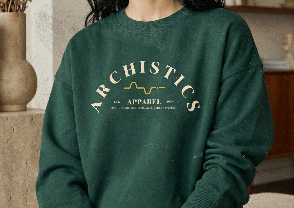 Woman wearing a green sweatshirt with 'ARCHISTICS APPAREL' text, sitting in a room with decor.